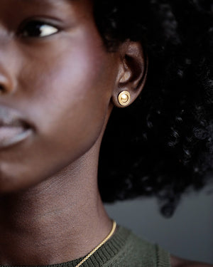 Woman wears pair of 12mm round gold studs; solid 18k gold.
