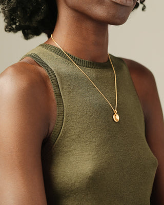 Black woman in a green sweater tank wearing a polished gold pendant necklace with a smooth, oval disc pendant hanging from a gold chain.