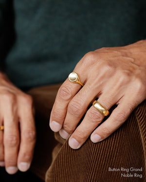 Cropped image of man's hands wearing gold rings. Large 18k yellow solid gold signet style ring with a large soft concave button circle atop the signet.