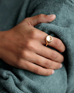 Cropped image of Woman's hands wearing gold rings. Large 18k yellow solid gold signet style ring with a large soft concave button circle atop the signet.