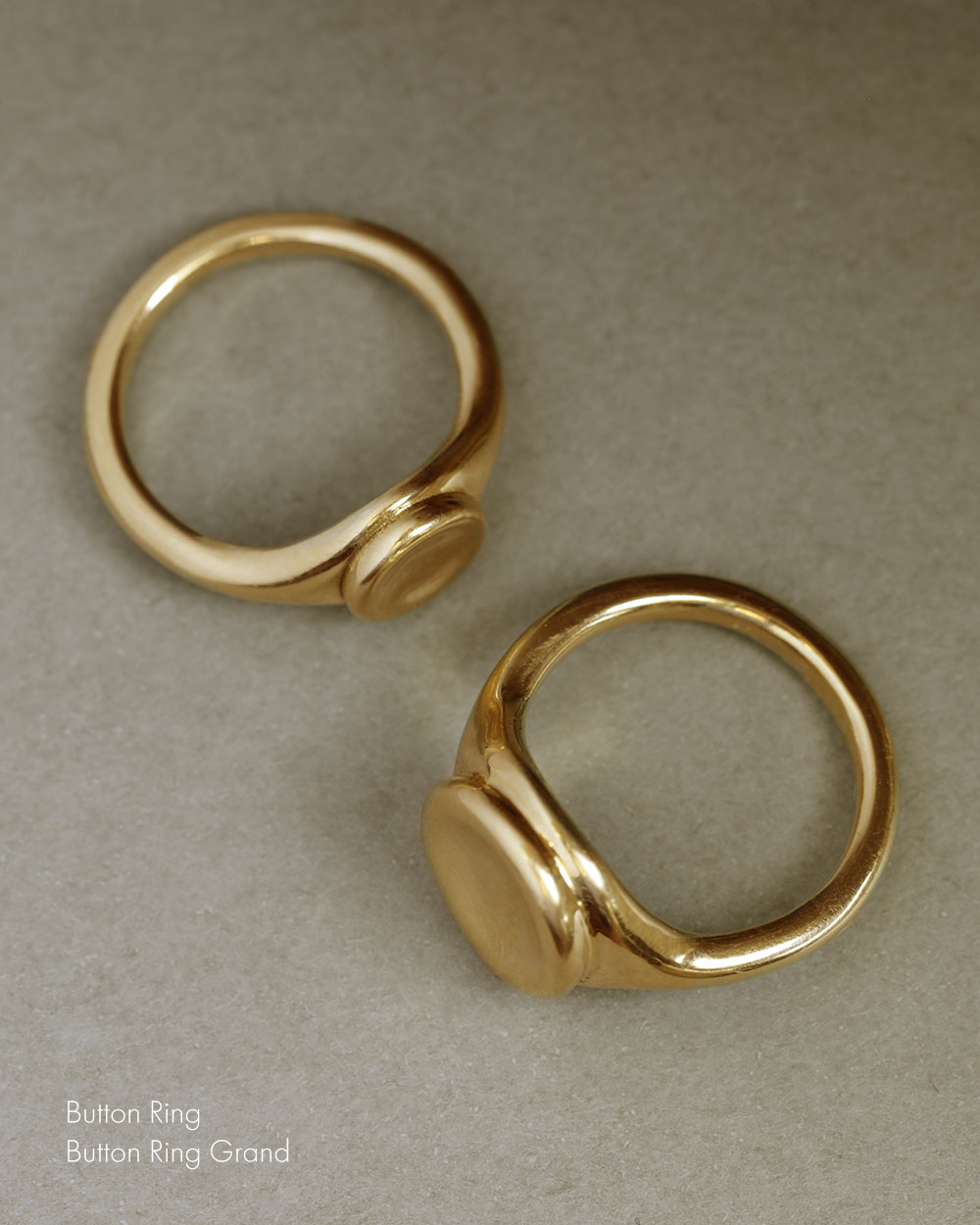 Top down view of two 18k gold button rings - one large and one small. Both 18k yellow solid gold signet style rings with a large soft concave button circle atop the signet.