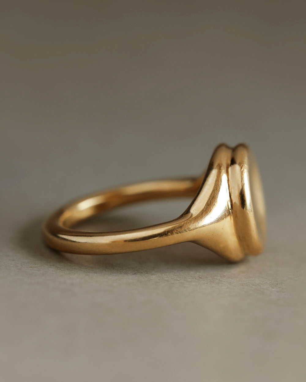 Profile view of a large 18k yellow solid gold signet style ring with a large soft concave button circle atop the signet.