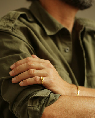 Close-up of a person wearing 18K gold rings on corduroy pants with a neutral background. Button Ring as a pinky ring.