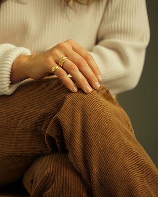 Close-up of a person wearing 18K gold rings on corduroy pants with a neutral background