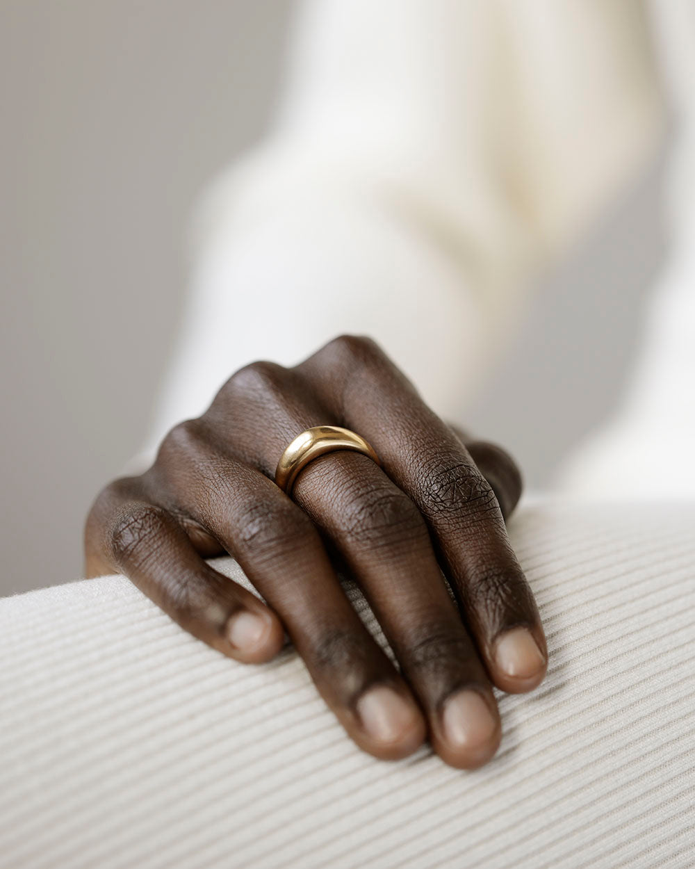 Woman's hand on white dress, wearing solid 18k yellow gold dome-shaped ring for weddings and milestones. Soft curves. Heavy.