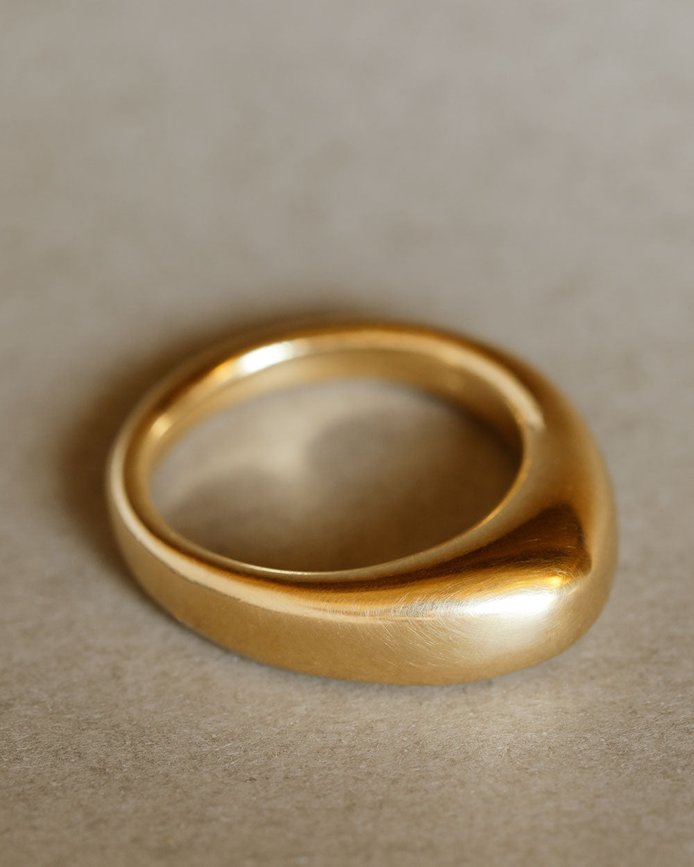 Solid 18k yellow large gold dome ring for weddings and milestones, lying flat on gray paper. Soft curves. Heavy. Not hollow.