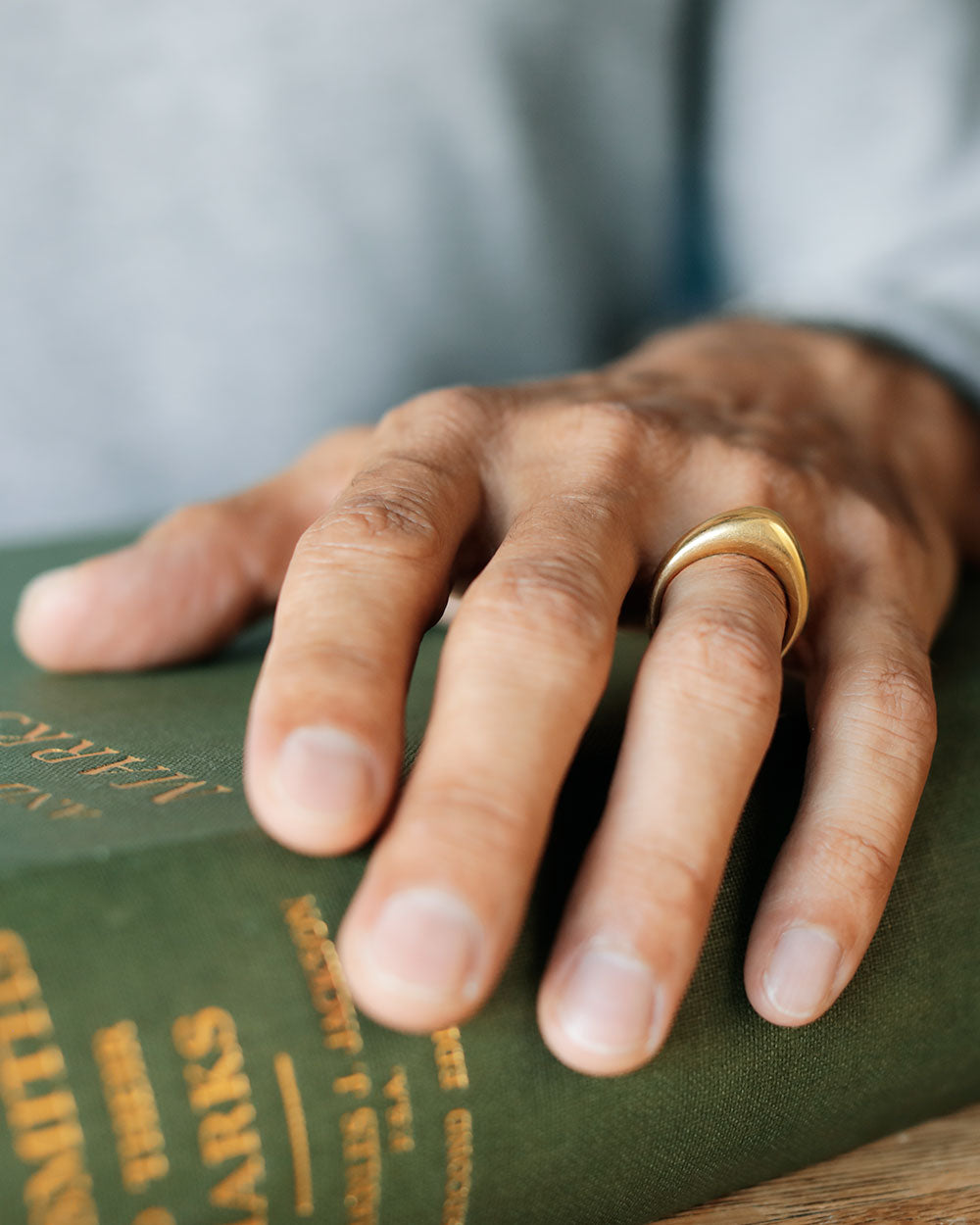 Man's hands on a green book, wearing solid 18k yellow large gold dome ring for weddings and milestones. Soft curves. Heavy. Not hollow.