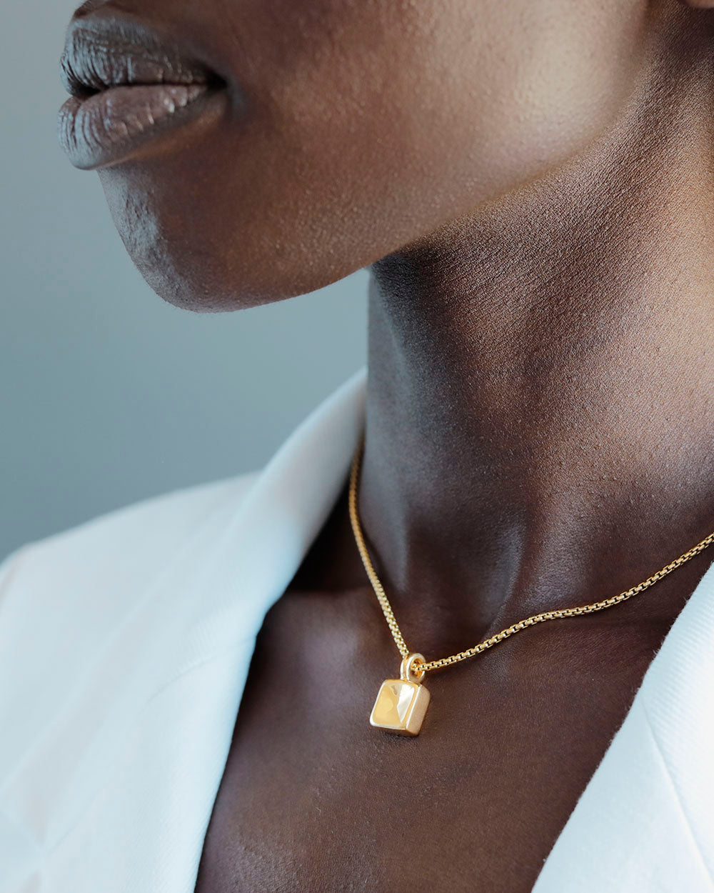 black woman in white blazer wearing chubby square pendant by george rings solid 18k gold nugget charm on round box chain