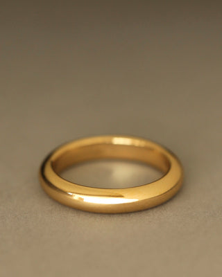 Round donut-shaped solid 18k yellow gold wedding band on gray paper. Dominus Band by George Rings.