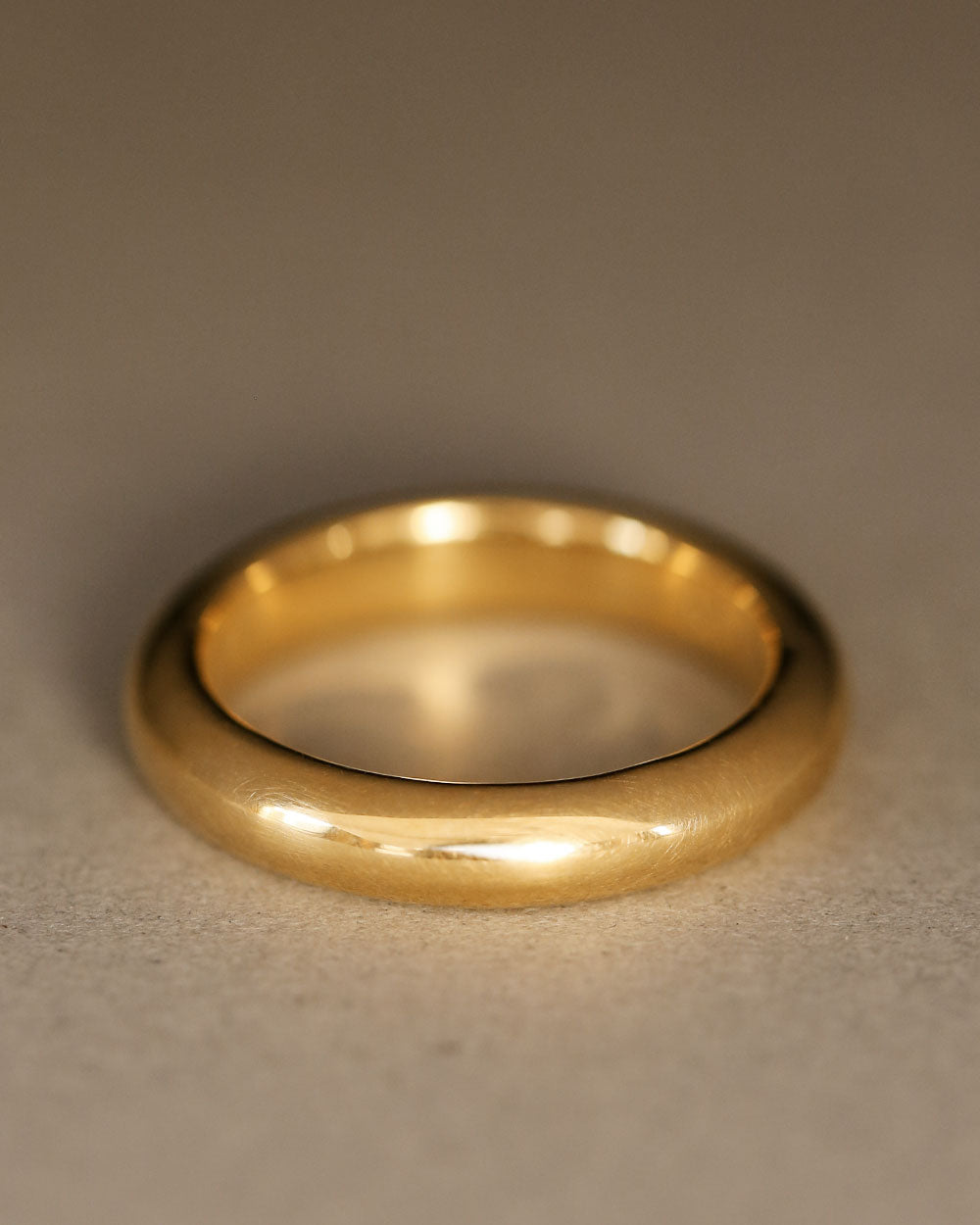 Round donut-shaped solid 18k yellow gold wedding band on gray paper. Dominus Band by George Rings.