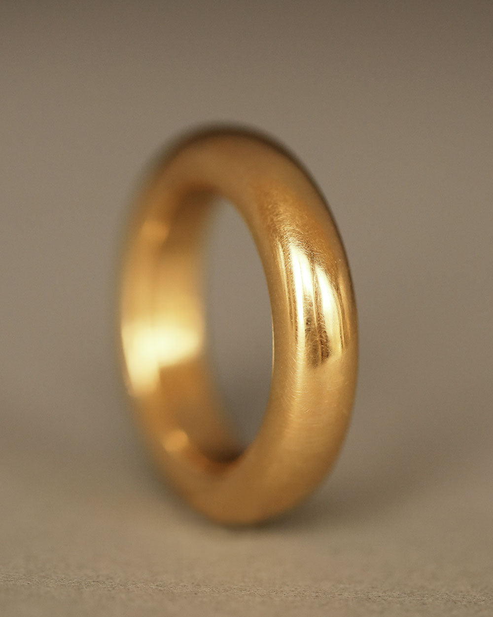 Large 18k solid yellow gold donut ring on gray paper. By George Rings. Dominus Band Grand