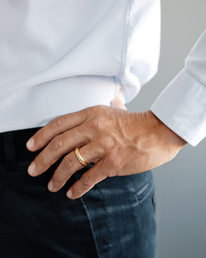 Man's hand on his green wool pants, with a Large 18k solid yellow gold donut wedding band on his ring finger