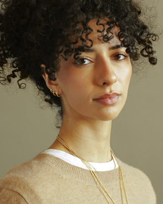 Dominus Hoops by George Rings. Model with curly hair wearing three sizes of hoops on one lobe - small, medium, large.