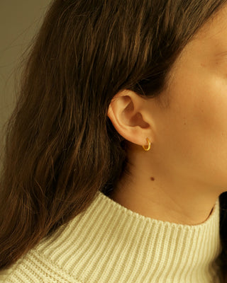 Close-up of an ear wearing a gold earring with a blurred background