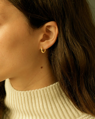 Close-up of an ear wearing a gold hoop earring with a blurred background