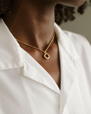 Woman in white collared shirt wearing solid 18k yellow gold donut pendant hanging on a 14k gold box chain. Soft and heavy.