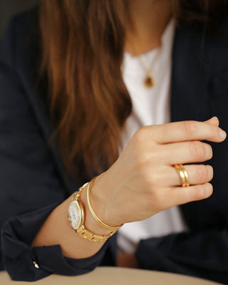 Close-up of a woman's hand wearing an Essential Cuff Bracelet by George Rings made of solid 18K yellow gold and paired with a Cartier ballon bleu watch