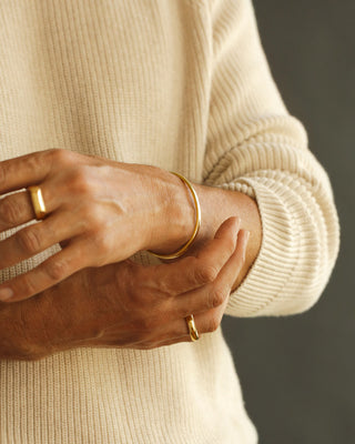 Close-up of hands wearing gold rings and a bracelet on a neutral background