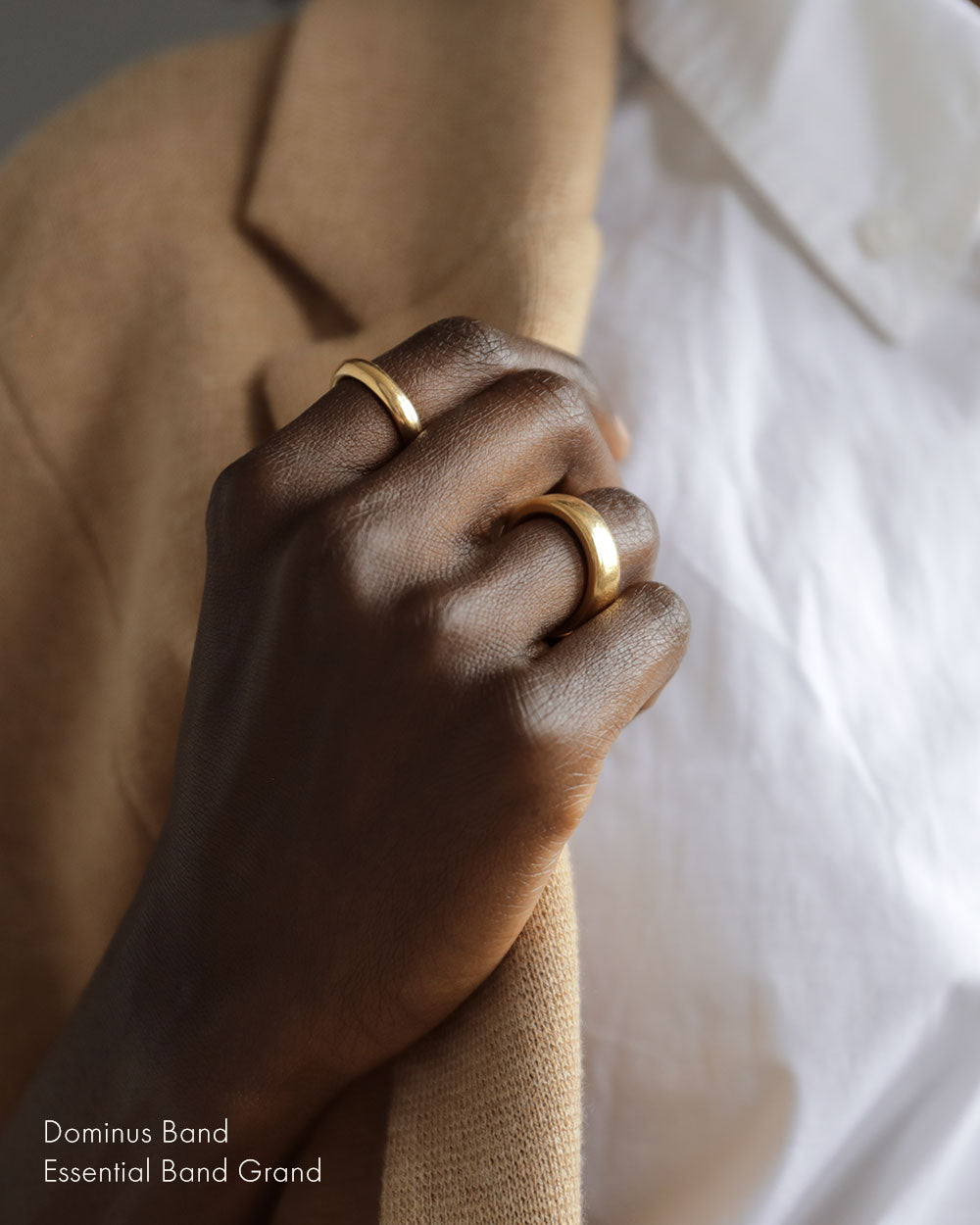 Woman wearing solid 18k yellow gold slim donut-shaped band on her index finger and large heavy rounded square 18k yellow gold band on ring finger. Essential Grande Band and Dominus Band by George Rings.