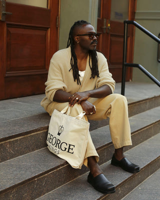 Person sitting on steps holding a tote bag with 'GEORGE RINGS' branding