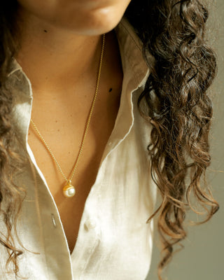 A close-up of a woman wearing a round box chain chain necklace in gold with a single 12mm south sea pearl pendant, handmade by George Rings.