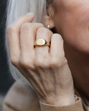 White woman holds hand near her face and wears Solid 18k yellow gold heavy signet wedding band on her ring finger. Hugo Signet Ring by George Rings.