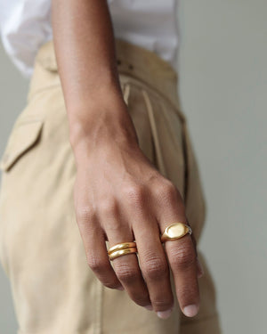 Woman holds hand in front of her. Two solid yellow 18k gold rings on her hand. She wears Solid 18k yellow gold heavy signet ring on her index finger Hugo Signet Ring by George Rings. She wears wedding band on her ring finger.
