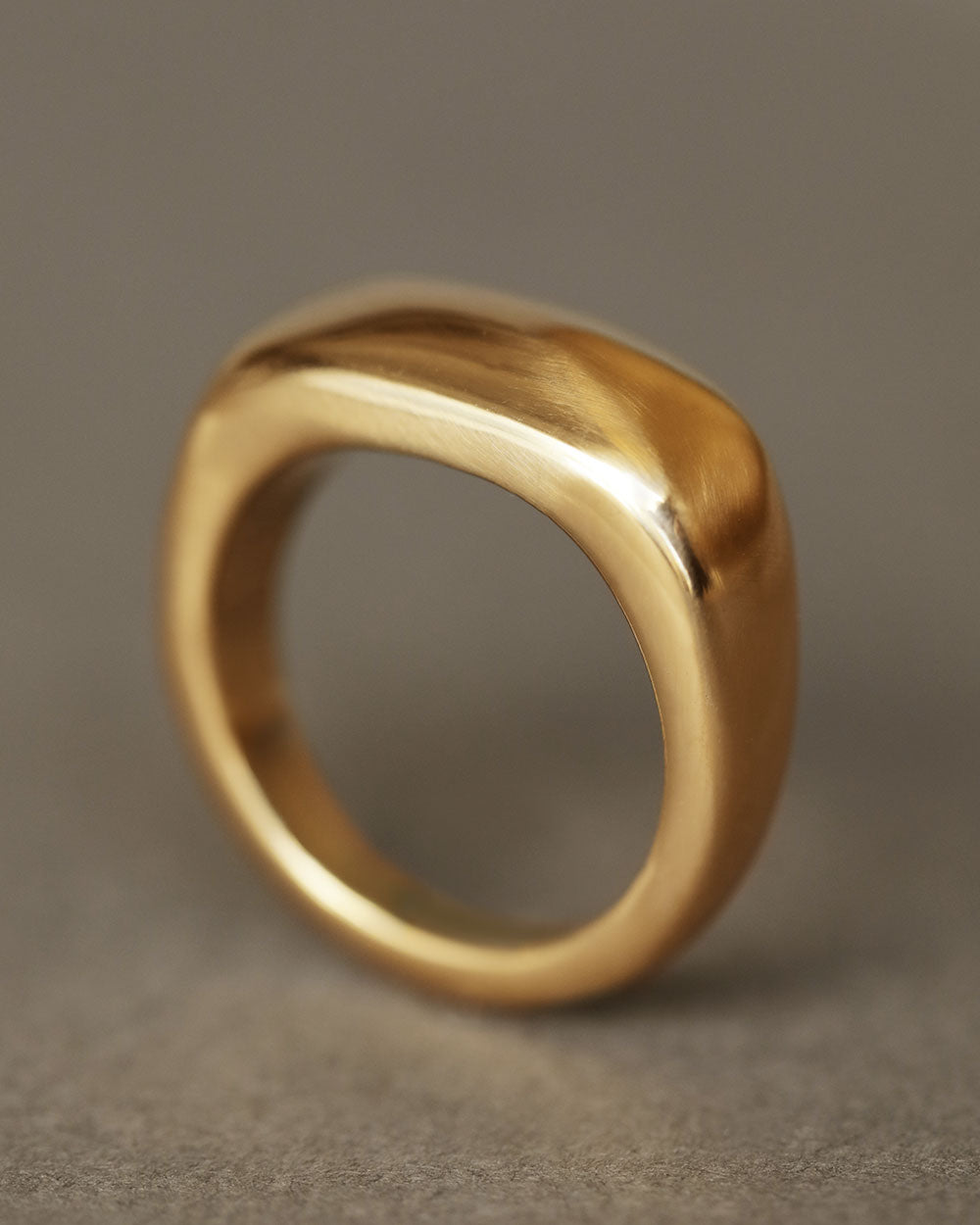Solid 18k yellow gold heavy ring upright on gray paper. Noble Ring by George Rings for men, women, and all genders.