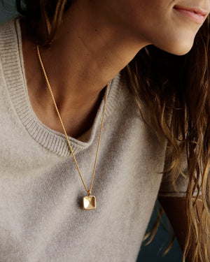 Woman wears a wool camel cashmere sweater and a solid 14k yellow gold box chain with solid heavy 18k yellow gold pillow pendant by George Rings yellow gold in size 20" with a lobster clasp.