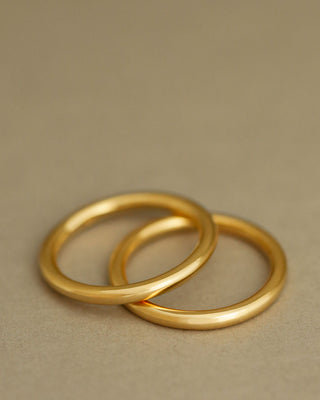 Two simple polished gold bands rings resting on a textured beige surface. Rae Band by George Rings, cast in solid 18K yellow gold.