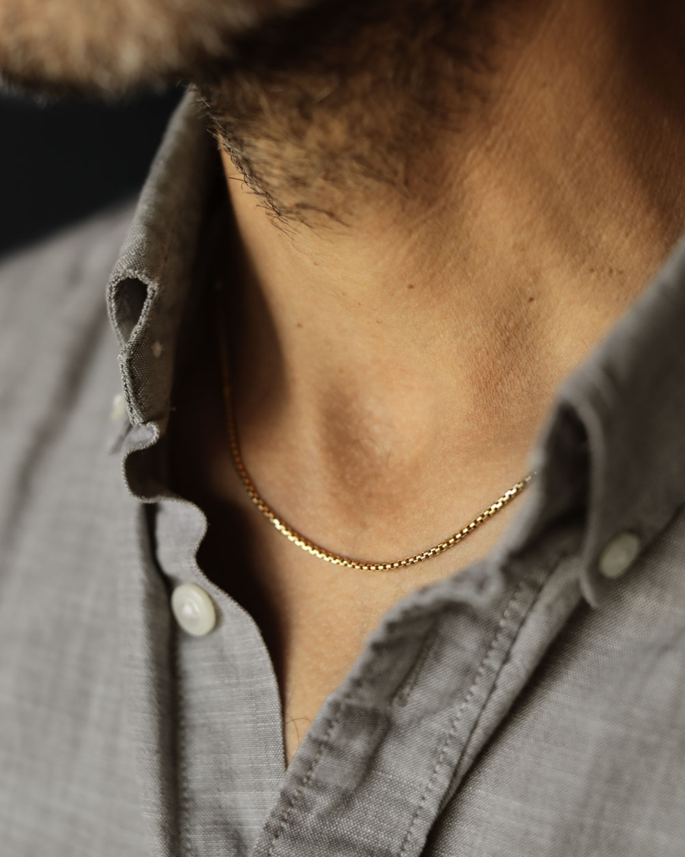 Man's neck and denim collared shirt with a solid yellow gold box chain by George Rings 14k yellow gold in size 16" with a lobster clasp.