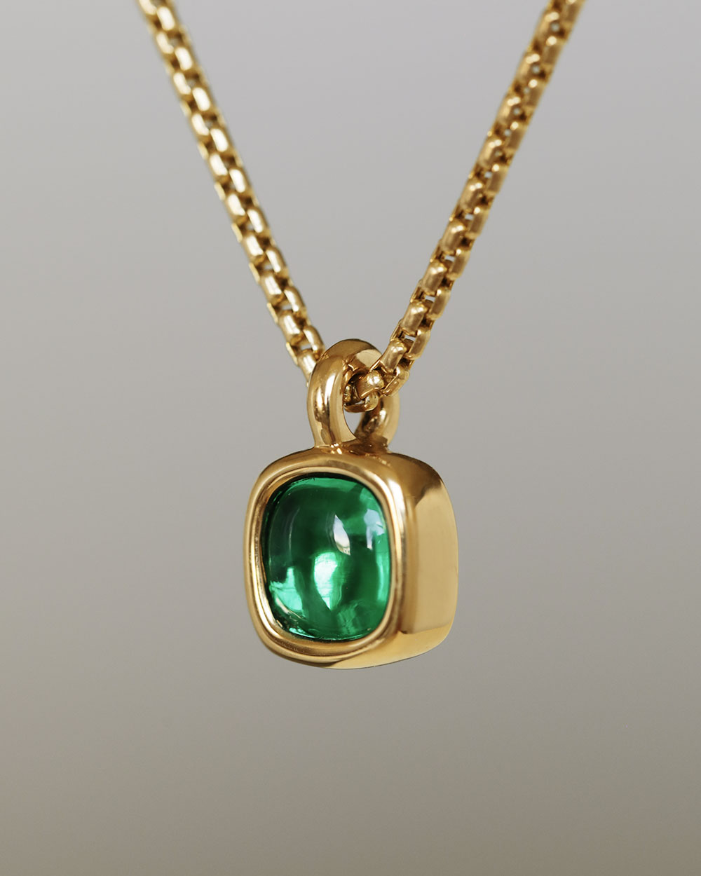 A juicy green lab grown emerald rounded square gem inside a solid 18k yellow gold bezel, hanging on a solid 14k yellow gold box chain. Sovereign Pendant by George Rings.