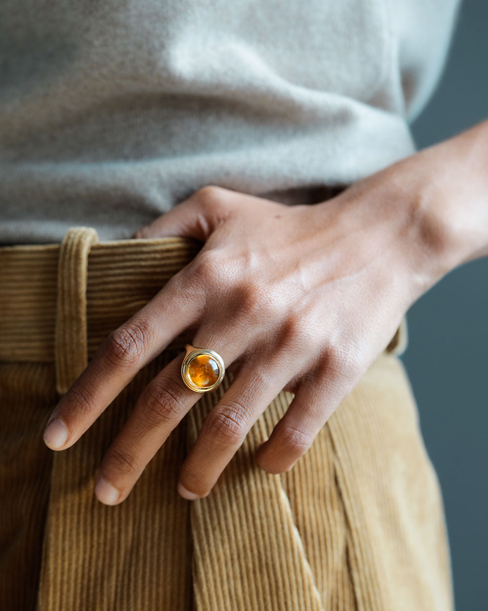 Woman's hand on her camel blazer wearing golden large round cabochon citrine gem sits inside large round 18k solid yellow gold signet ring. The Monarch by George Rings.