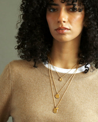 Woman wearing a beige sweater and gold necklaces with a neutral background