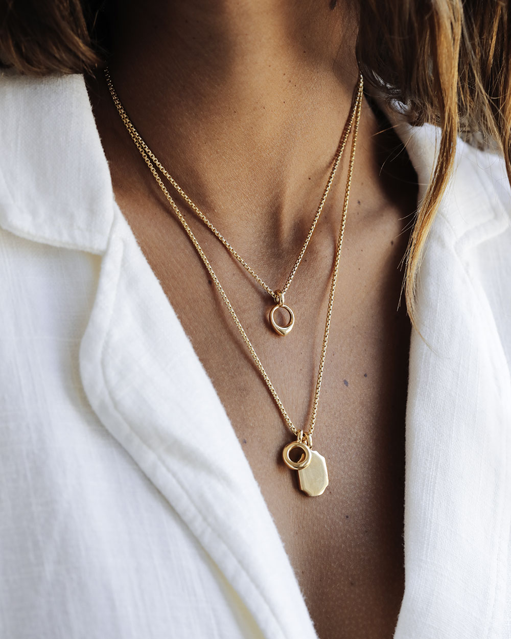 Woman wears a white linen blazer and layered chains; Golden 8 sided pendant with large bail and chain. Solid 18k gold, thick and substantial. Round box cut 14k gold chain.
