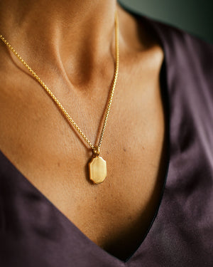Woman wears  v-neck silk shirt and gold 8 sided pendant with large bail and chain. Solid 18k gold, thick and substantial. Round box cut 14k gold chain.