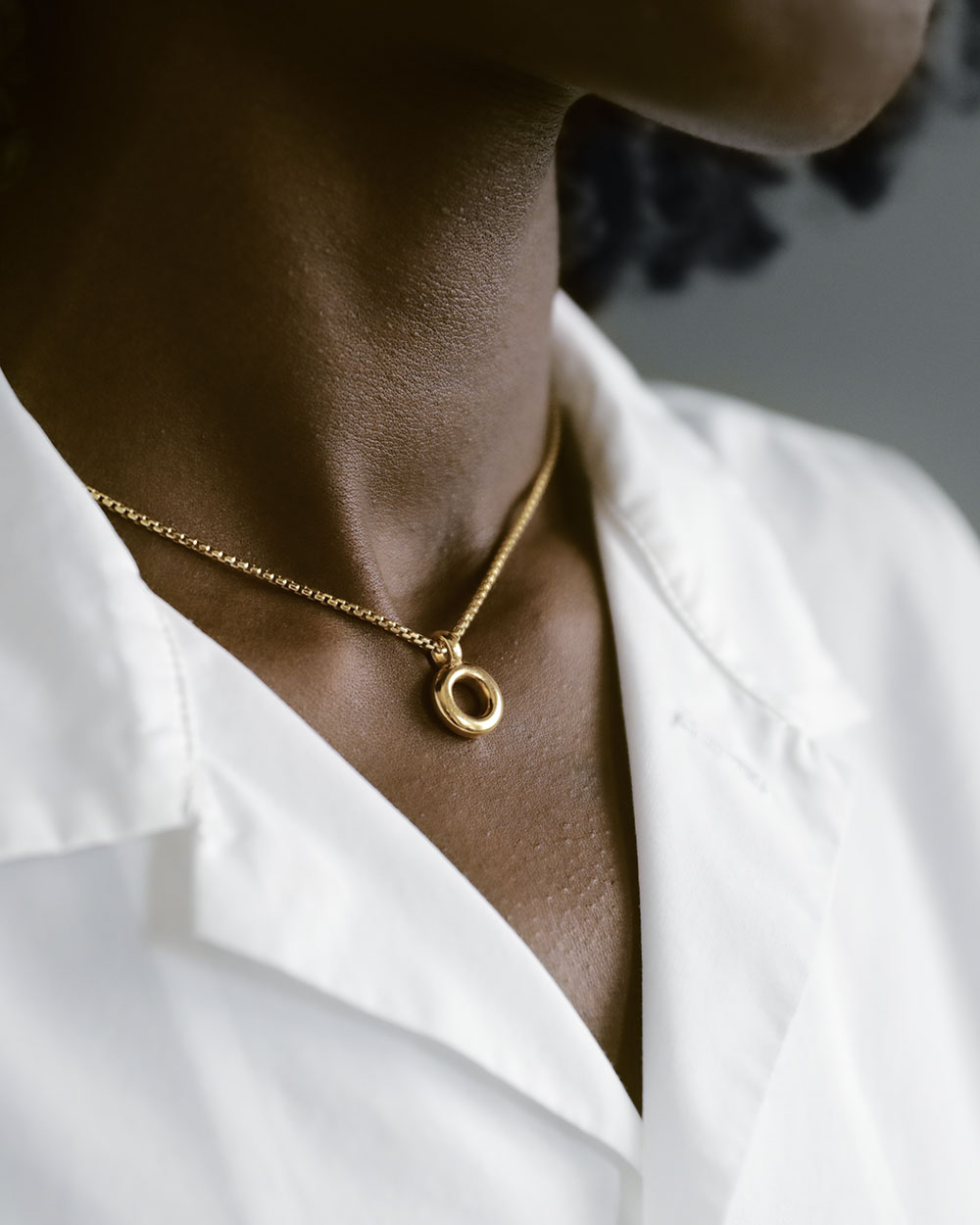 Woman in white collared shirt wearing solid 18k yellow gold donut pendant hanging on a 14k gold box chain. Soft and heavy.