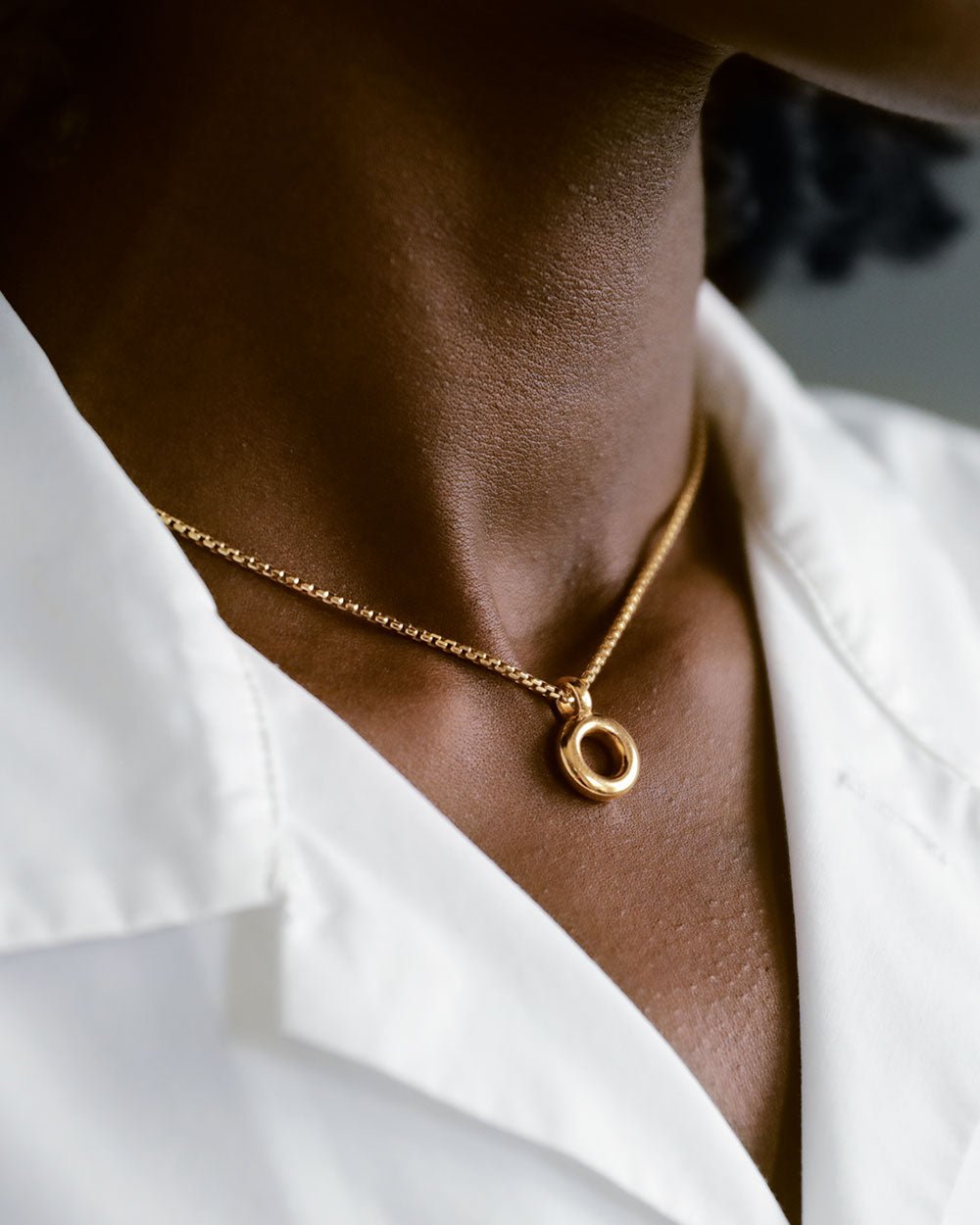 Woman's neck and white collared shirt with a 14k solid yellow gold box chain with yellow 18k gold donut pendant by George Rings in size 16" with a lobster clasp.