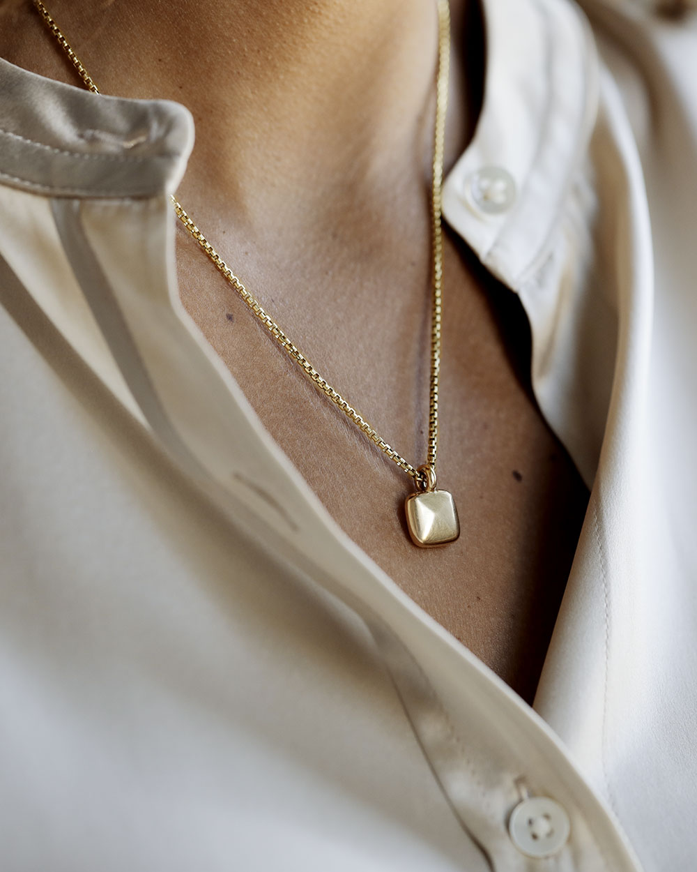 Woman wears solid 18k yellow gold pillow pendant on a solid 14k yellow gold box chain. Pillow Pendant by George Rings.