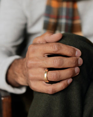 Man's hand on green wool pants. He is wearing heavy mens wedding band in solid 18k yellow gold, laying on gray paper. Essential Grande Band by George Rings.