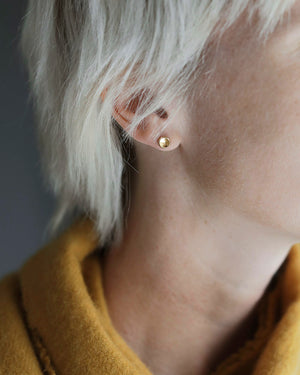 Woman's head and ear wearing pair of solid 18k yellow gold stud earrings, shaped as concave substantial little buttons