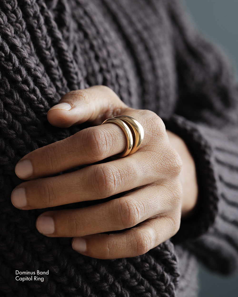 Woman wearing solid 18k yellow gold slim donut-shaped band on her index finger and large heavy rounded square 18k yellow gold band on ring finger.
