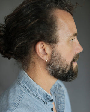 Man's head with curly hair and beard, wearing Pair of solid 18k yellow gold hoop earrings with a soft dome shape. Part of the George Rings Capitol Collection.