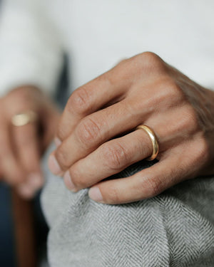 Man's hand on herringbone wool pants, wearing solid 18k yellow gold slim donut-shaped wedding band.