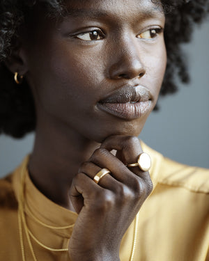 Young black woman smiles and wears a solid 18k yellow gold Dutch Coin ring. Large circle of gold with a slight puff in the center and softened, thick edges. 