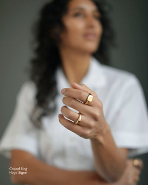 Woman holds hand near her face and wears Solid 18k yellow gold heavy signet wedding band on her ring finger. Hugo Signet Ring by George Rings.