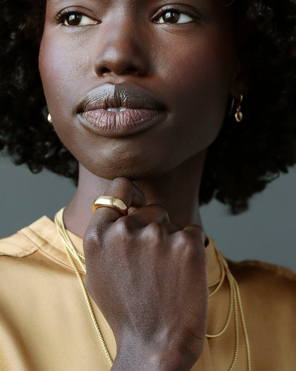 Black woman with hand on her chin, wearing Solid 18k yellow gold heavy wedding band on ring finger. Noble Ring by George Rings for men, women, and all genders.