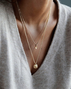 Woman wears solid 18k yellow gold pillow pendant on a solid 14k yellow gold box chain. Pillow Pendant by George Rings.